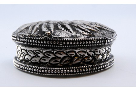 Caixa de comprimidos em prata de forma circular com motivos vegetalistas relevados na tampa amovível.